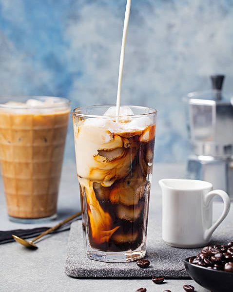 An iced coffee with milk being poured in